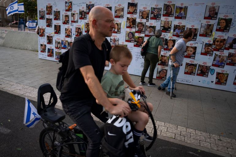 Un uomo passa in bicicletta davanti a un muro con le foto degli ostaggi