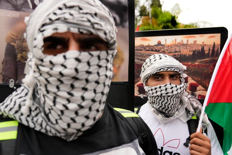 Protesters, their faces wrapped in keffiyeh scarves, protest in front of screens outside the French embassy in Beirut.