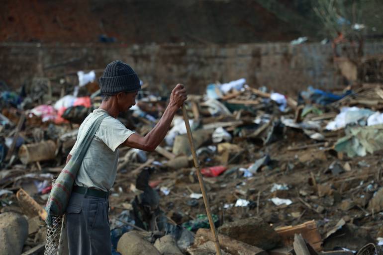A man looking at the destruction caused by the military attack. Debris is strewn across the ground.
