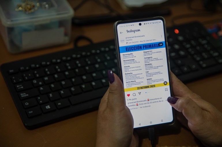 Two hands hold up a lit-up cellphone, where an Instagram post shows a graphic with polling centre information for the Venezuela opposition vote.