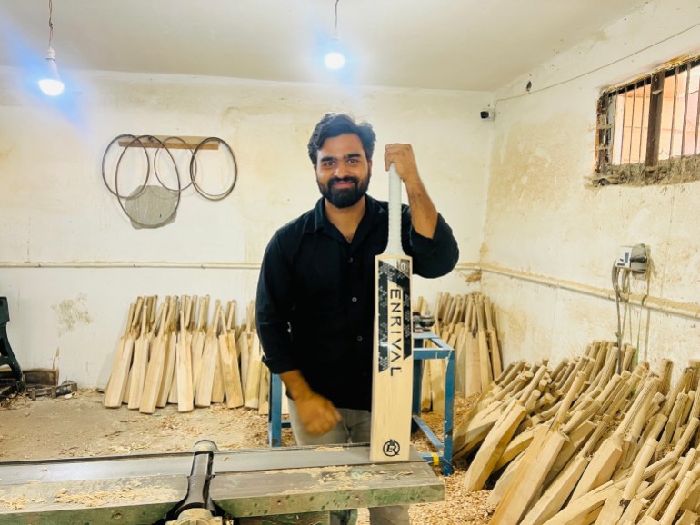 Faizan Mir holds a cricket bat and smiles at his bat manufacturing factory in Pampore in the southern part of Kashmir
