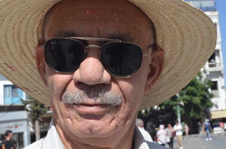 A man in dark sunglasses and a wide-brimmed straw hat on the streets of Tunis.