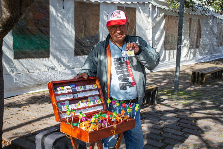 A street vendor holds up a card with one hand and holds open a briefcase with merchandise with the other.