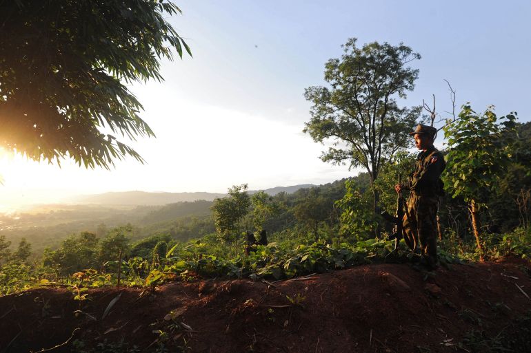 A view of Kachin rebel area near the Chinese border. It's green and hilly. There's a soldier silhouetted to the right.