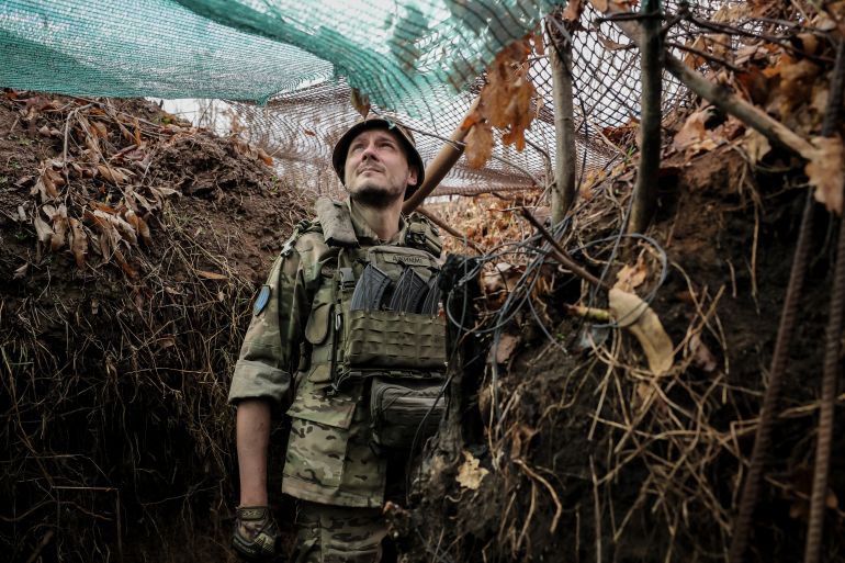 A Ukrainian brigade commander standing in a trench on the eastern front line. There is camouflage netting above him