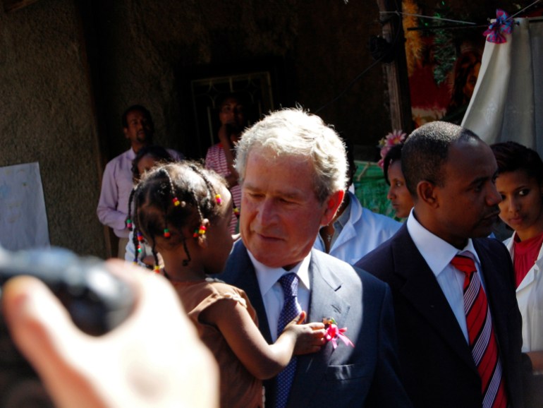 George W Bush, dressed in a suit and tie, holds a baby girl during his visit to Ethiopia.