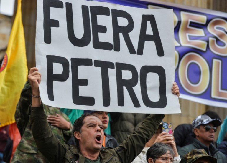 A man dressed in military fatigues holds up a sign that reads, "Fuera Petro," as he shouts.