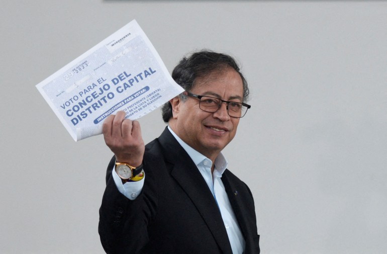 Colombian President Gustavo Petro, wearing a dark suit and a white collared shirt, holds up a ballot during the October 29 elections.