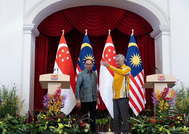 Les premiers ministres de Singapour et de Malaisie lors de leur retraite à Singapour.  Ils se tiennent devant les drapeaux de leur pays.