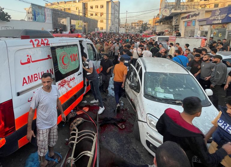A stretcher likes on the ground near a convoy of white vehicles and ambulances as crowds rush to assist in the wake of a bomb blast.