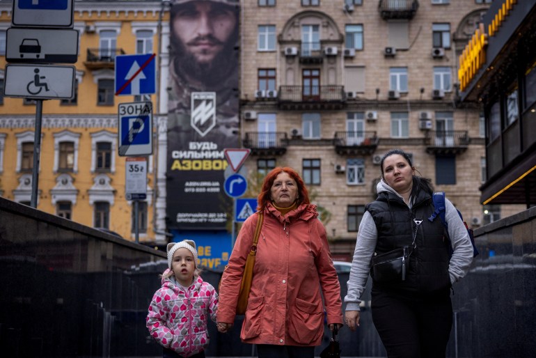 Women and a child walk near a recruitment poster for the Azov Assault Brigade of the National Guard of Ukraine, amid Russia's attack on Ukraine, in Kyiv, Ukraine, November 8, 2023. REUTERS/Thomas Peter