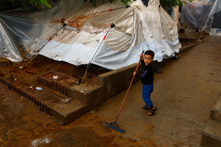 A child squeeges rain water as displaced Palestinians shelter in a tent camp, amid the conflict between Israel and Palestinian Islamist group Hamas