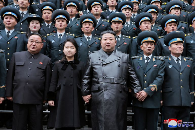 Kim Jong Un com cientistas e engenheiros que contribuíram para o lançamento do satélite espião na terça-feira.  Ele está parado na frente com sua filha ao lado dele.