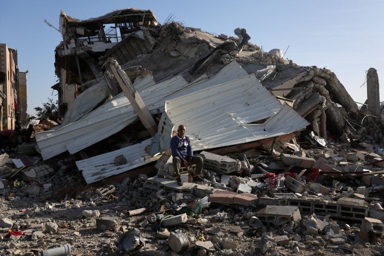 A Palestinian man sits on the rubble of a destroyed house