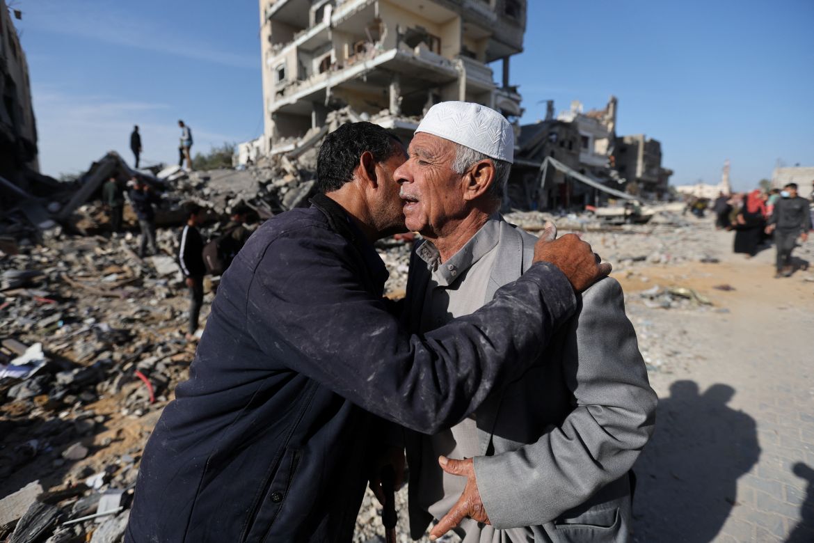 Palestinian men embrace each other near a house destroyed in an Israeli strike during the conflict, amid the temporary truce between Hamas and Israel, in Khan Younis