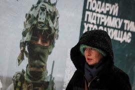 A woman walks past a poster depicting a Ukrainian serviceman as snow falls in Kyiv [Gleb Garanich/Reuters]
