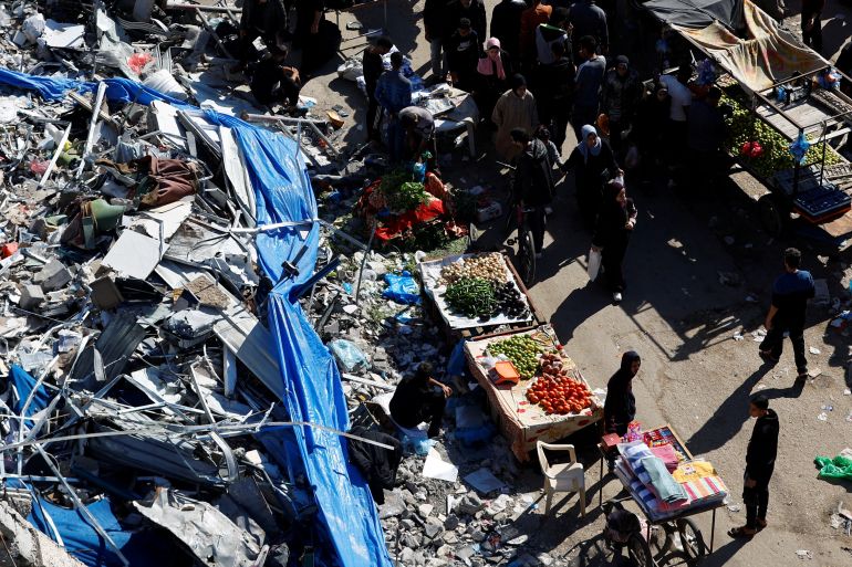 Palestinians shop near the ruins of houses and buildings destroyed in Israeli strikes