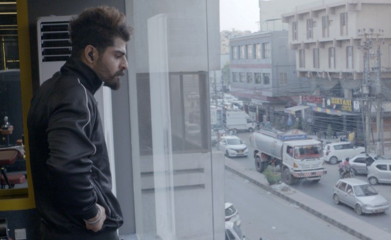23. Usama looks out a gym window overlooking a busy commercial area in Karachi