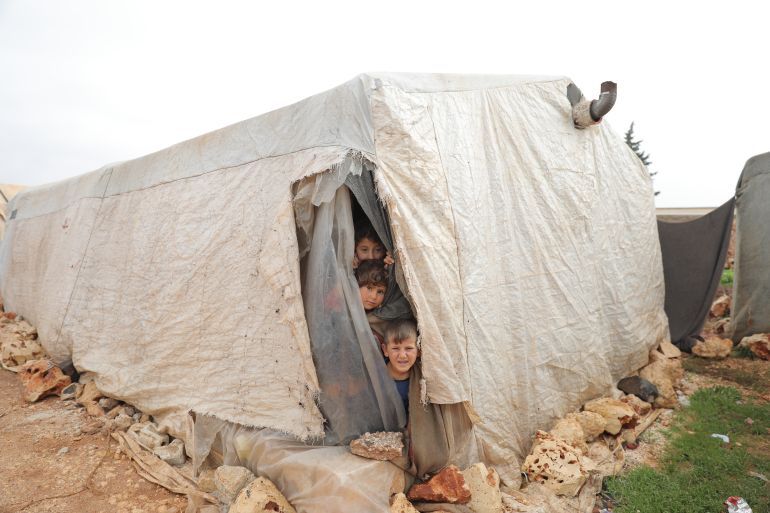 Children look out of a tent housing a family at Kafr Yahmul camp