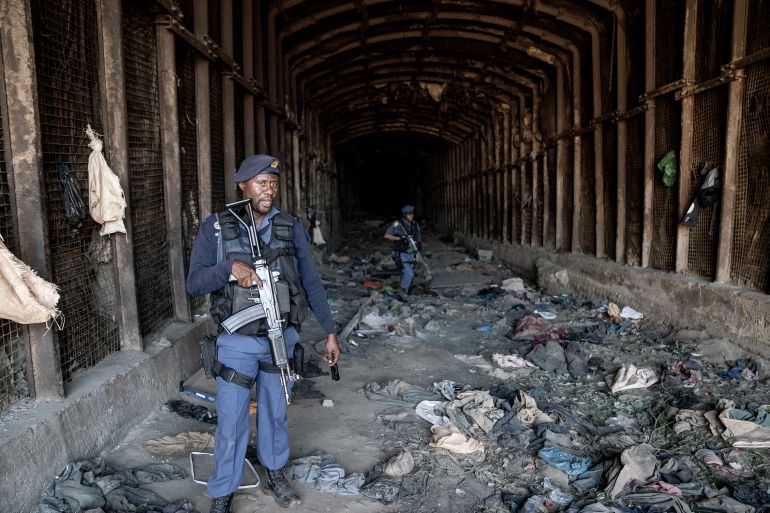Members of the South African Police Service (SAPS) carry their weapons as they guard the entrance to an abandoned mine during an operation in Stormhill west of Johannesburg on August 10, 2023 where territorial battles between illegal miners known as Zama Zamas has wreaked havoc in the area claiming the lives of several miners. Five people have been shot dead in South Africa's Johannesburg in suspected violence between rival illegal mining gangs, police said Sunday. The five bodies, believed to be of illegal miners, were found near an abandoned mine shaft clsoe to a slum in the suburb of Riverlea west of Johannesburg. (Photo by Shiraaz Mohamed / AFP)