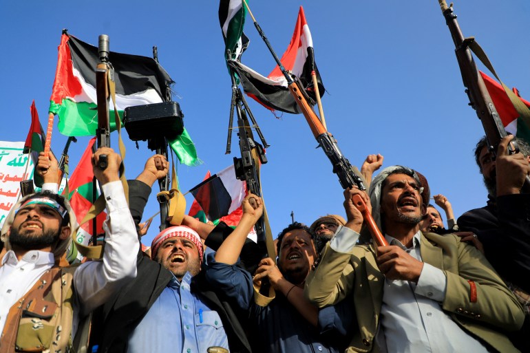 People brandish rifles and Palestinian flags during a march to show solidarity with the Palestinians of the Gaza Strip on October 18, 2023, in the Houthi-controlled Yemeni capital Sanaa