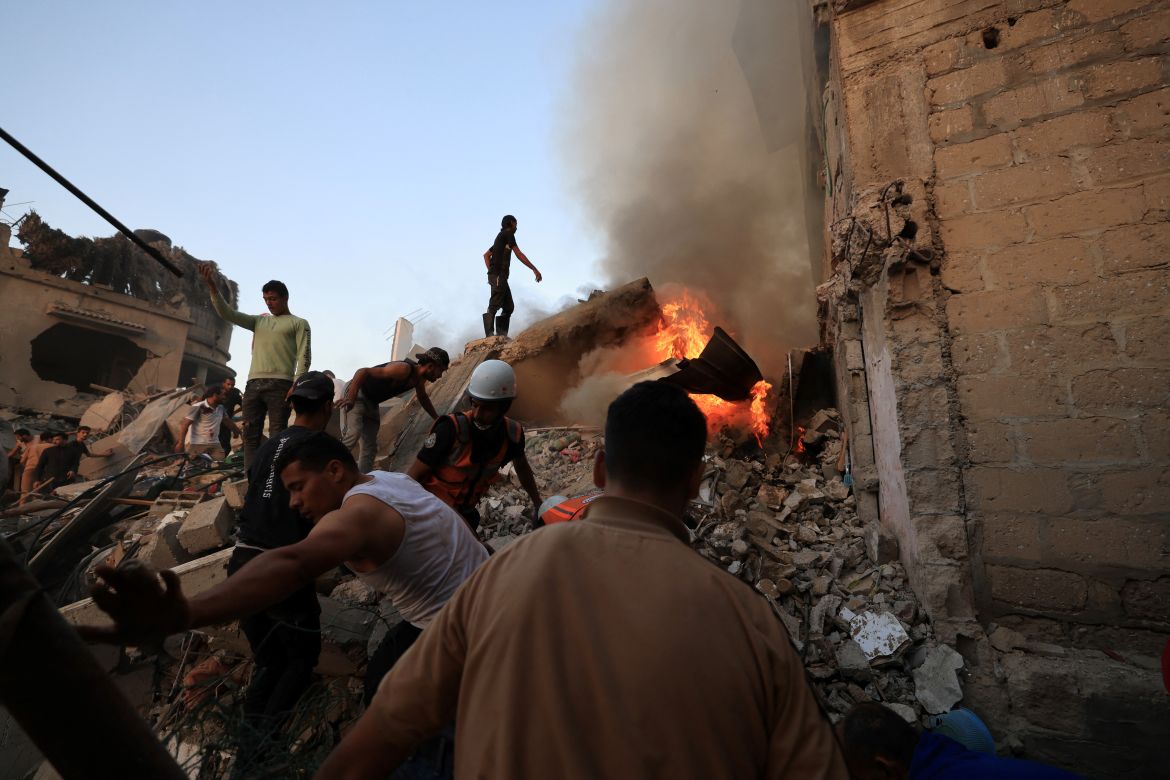 Palestinian rescuers attempt to put out a fire as they stand on the rubble of a collapsed building following a strike by the Israeli military on Khan Yunis