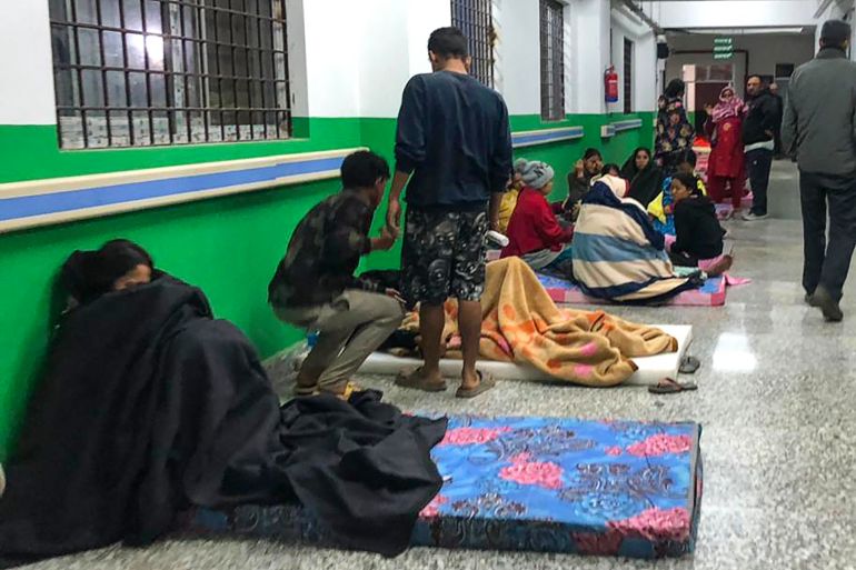 People in the corridors of the local hospital in Jajarkot after the earthquake. They are sitting along the wall. Some are standing.