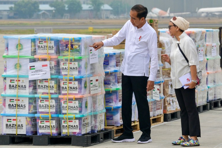 Joko Widodo examines aid intended for Gaza at the airport.  The aid is on pallets and ready to be put on the plane.  Widodo is accompanied by his Minister of Foreign Affairs