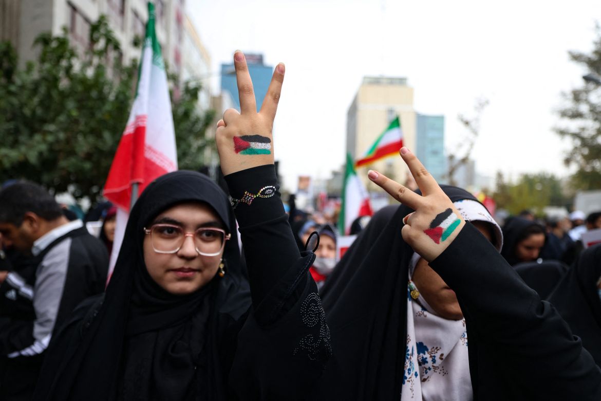 Iranian women with Palestinian flags painted on their hands flash the victory sign during a rally outside the former US embassy in Tehran, to support the Palestinians of the Gaza Strip and to mark the 44th anniversary of the start of the Iran hostage crisis.
