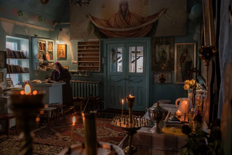 An elderly woman prays at a church in Posad-Pokrovske. There is a fresco above the door and icons on the walls. Candles are burning.