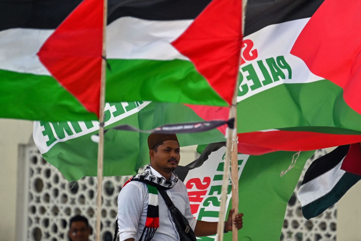 A man stands beside Palestinian flags during a rally in support of Palestinians in front of the Baiturrahman Grand Mosque in Banda Aceh.