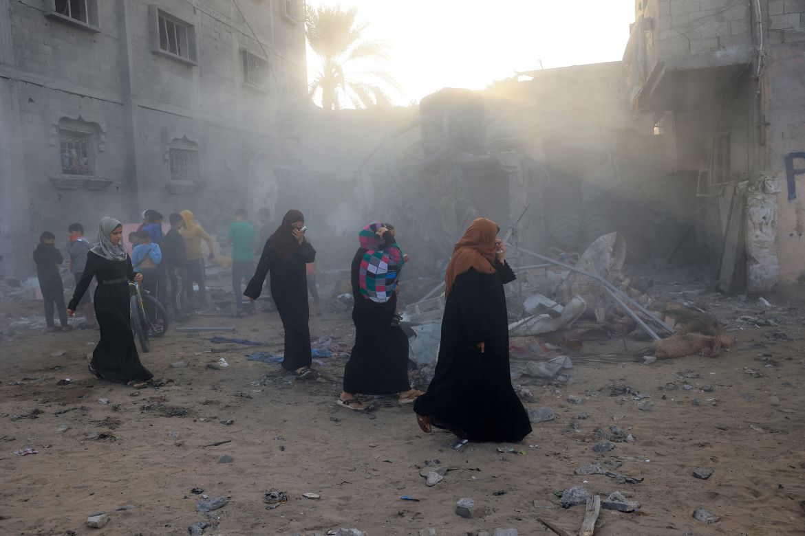 Women walk past the smouldering rubble of a destroyed building following Israeli bombing on Rafah in the southern Gaza Strip