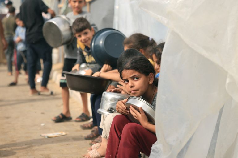 Internally displaced Palestinian children who have fled their homes in the northern Gaza Strip due to intense Israeli military bombardment, hold containers as they wait for food in Khan Younis