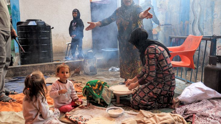 A woman reacts while another prepares traditional unleavened bread on an open fire at school run by the United Nations Relief and Works Agency for Palestine Refugees in the Near East (UNRWA) in Rafah in the southern Gaza Strip.