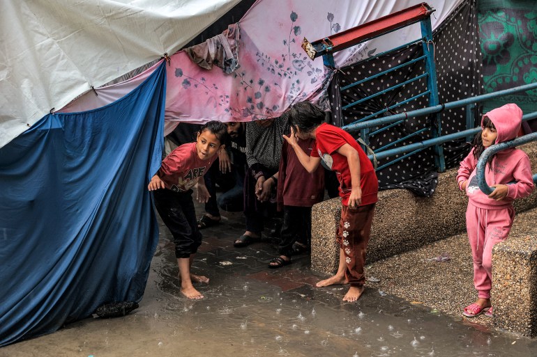 Children take shelter from the rain under a tent in Rafah in the southern Gaza Strip