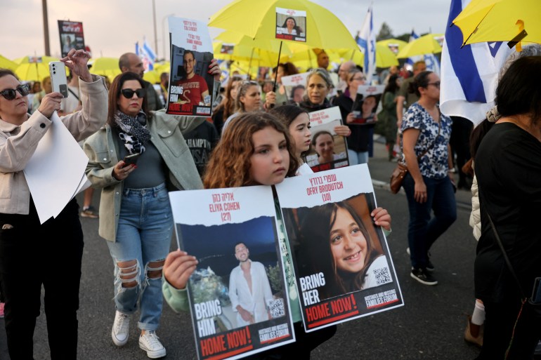 Une jeune fille porte des affiches représentant Eliya Cohen (à gauche), 27 ans, et Ofry Brodutch, 10 ans, toutes deux détenues par le Hamas à Gaza. [AHMAD GHARABLI / AFP]