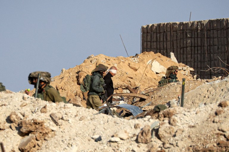 İsrail askerleri, 19 Kasım 2023'te, savaştan zarar gören Gazze'deki çatışmalardan kaçan Filistinlilerin Gazze Şeridi'nin güney kesimindeki Zeitoun bölgesindeki bir yolda yürüyüşünü izlerken, gözleri bağlı Filistinli erkekleri askeri bir kamyonda gözaltına alıyor.