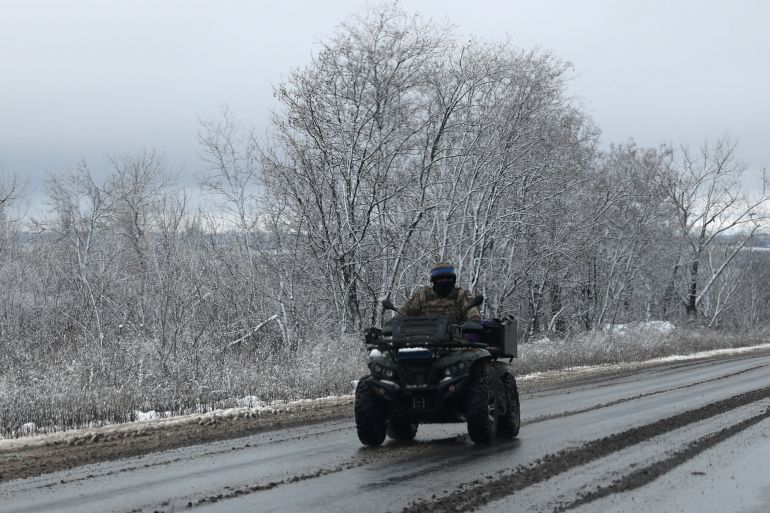 A Ukrainian soldier riding a quad bike on a slush covered road in Donetsk region. The trees behind are covered in snow