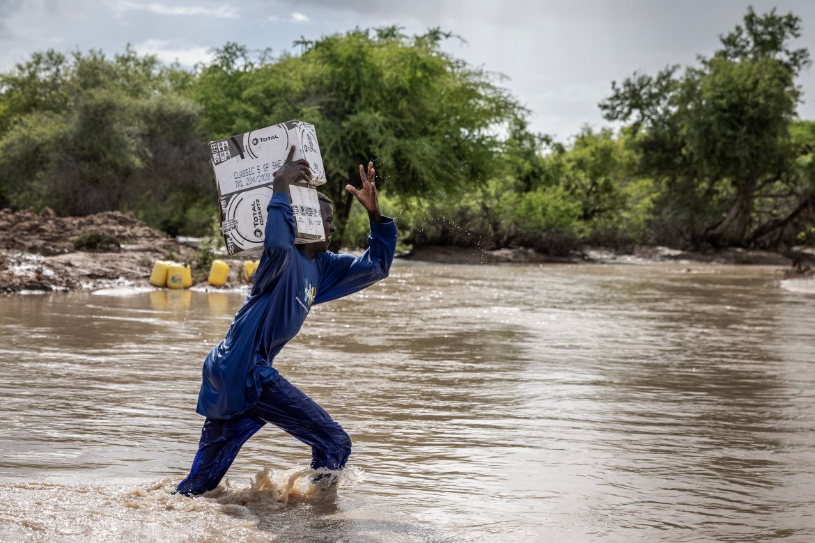 A man carries boxes with good while crossing a flooded area next to the section of a road destroyed by flash floods at the Garissa-Wajir Road in Maalimin.