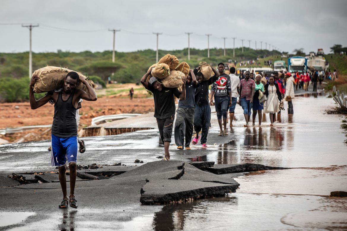 People carry their belongings while crossing the section of a road collapsing due to flash floods at the Mwingi-Garissa Road near Garissa.