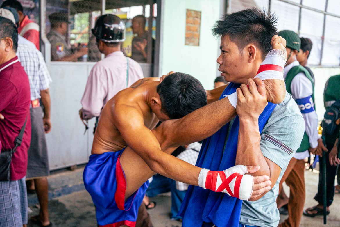 Power Punch coach Aung Lay stretches out Zaw Du La Mashi’s leg pre-fight. Squeezed between the ticket booth and the bag check, the fighters have little room to wrap their feet and fists in gauze, and massage and stretch out their muscles.
