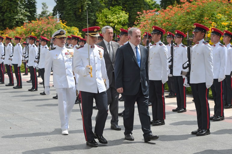 Benjamin Netanyahu tijdens een bezoek aan Sinapore in 2017. Hij wandelt met de premier van Singapore, Lee Hsien Loong.  Aan één kant staan ​​soldaten in witte ceremoniekleding.