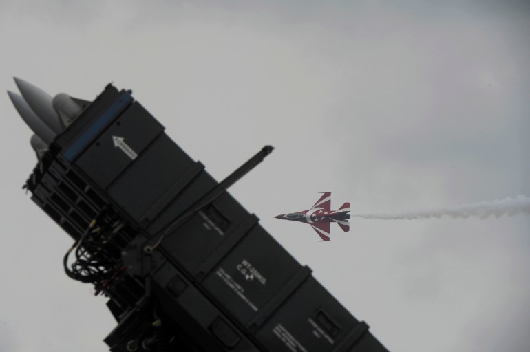 Um caça a jato de Cingapura pintado em vermelho e branco voa no ar atrás de um míssil superfície-ar Rafael no show aéreo de Cingapura.