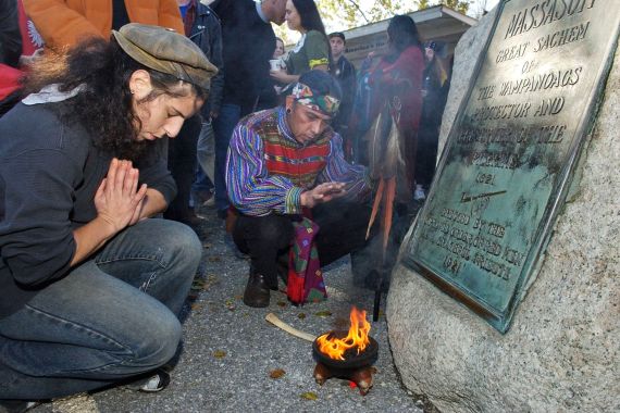 A man kneels in prayer on Cole's Hill in Plymouth, as a flame burns in front of a plaque turned green with age.