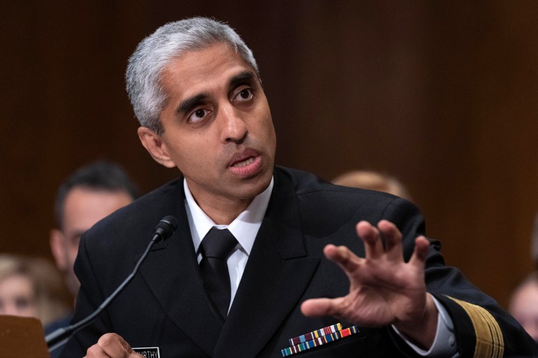 Vivek Murthy, wearing military dress uniform, gestures with one arm outstretched as he speaks into a microphone during a Senate hearing.