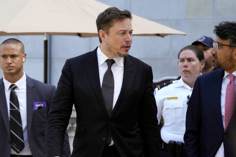 Elon Musk takım elbiseli insanlarla birlikte yürüyor