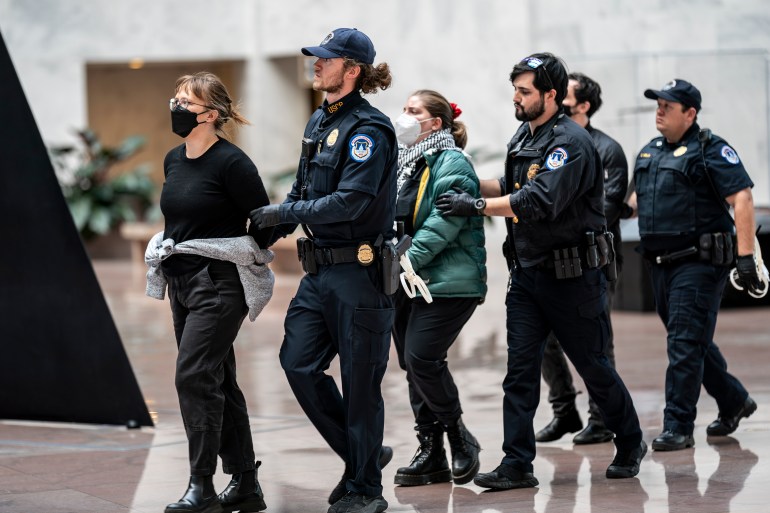 Due manifestanti, uno vestito con un piumino e l'altro con una maglietta nera, vengono portati via con le mani dietro la schiena dalla polizia del Campidoglio.