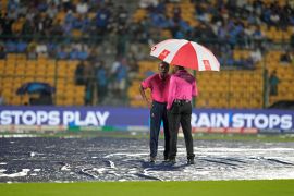 An umpire, right, stands on the pitch, covered with plastic sheets, after rain stopped play during the ICC Men's Cricket World Cup match between New Zealand and Pakistan in Bengaluru, India, Saturday, Nov. 4, 2023. (AP Photo/Aijaz Rahi)