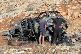 People stand next to the remnants of a car destroyed in an Israeli airstrike