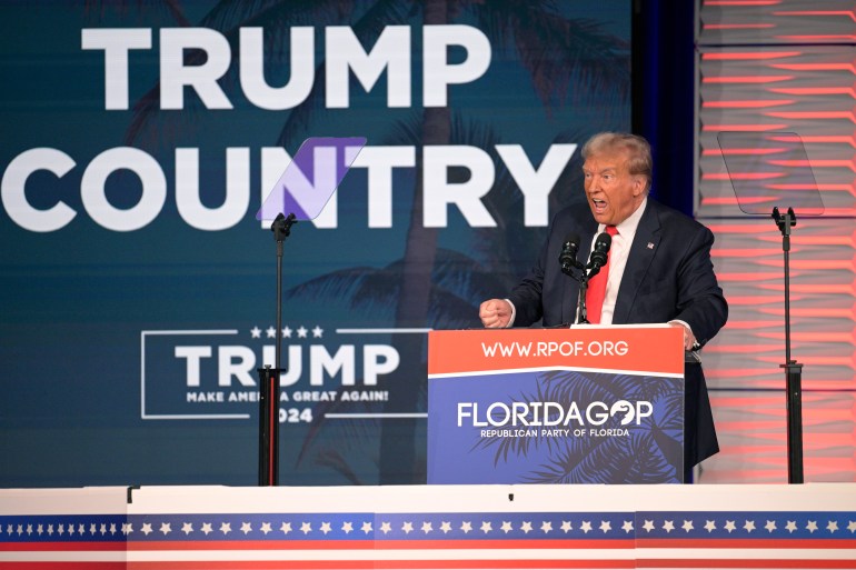 Donald Trump sta dietro un podio del GOP della Florida, parlando al pubblico.  Dietro di lui c